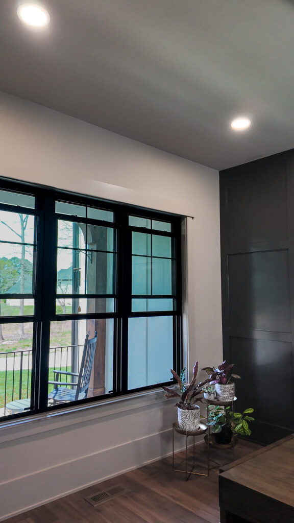 Three black double hung windows all opened to the front porch with a rocking chair.