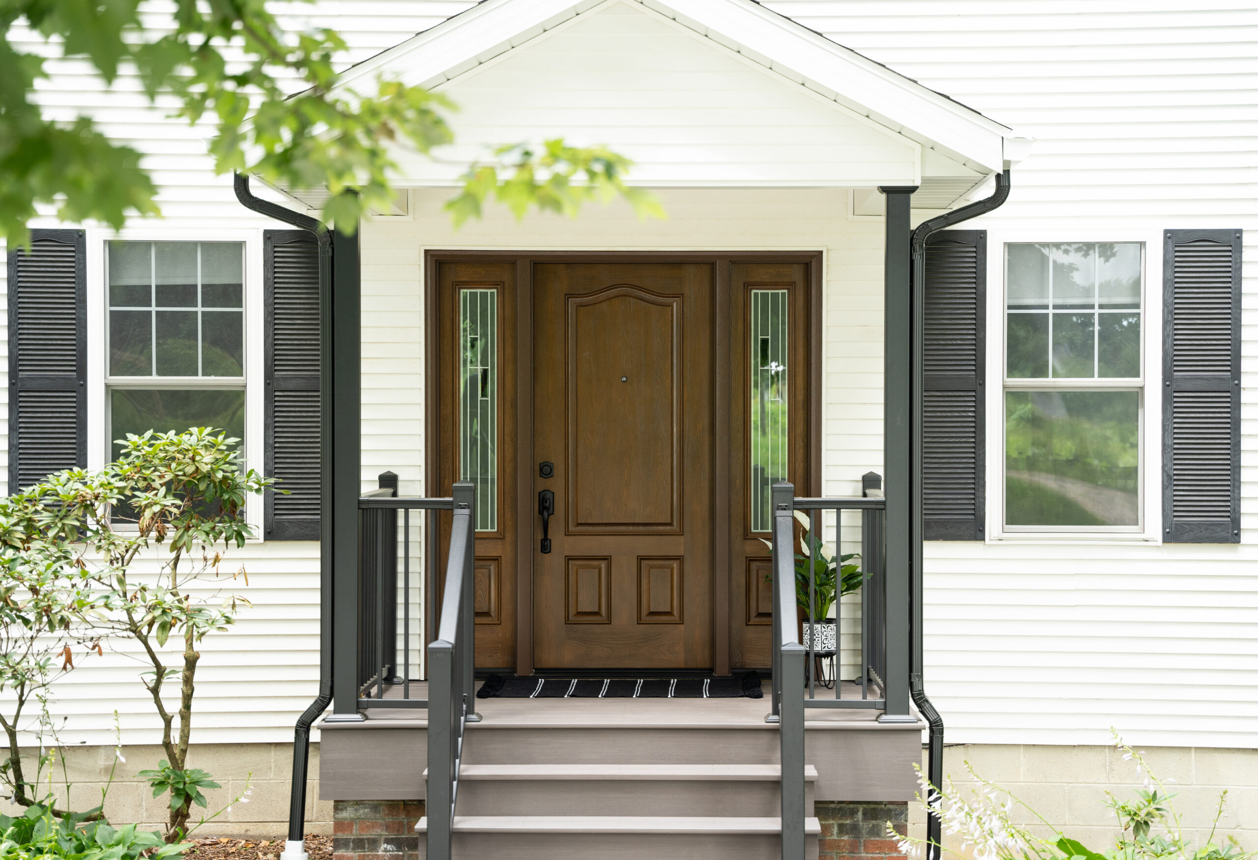 Brown entry door with white windows on either side of the front porch.