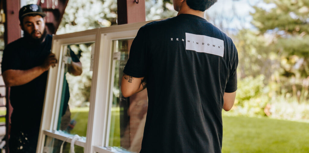 Two window installers carry a large window to the job site.