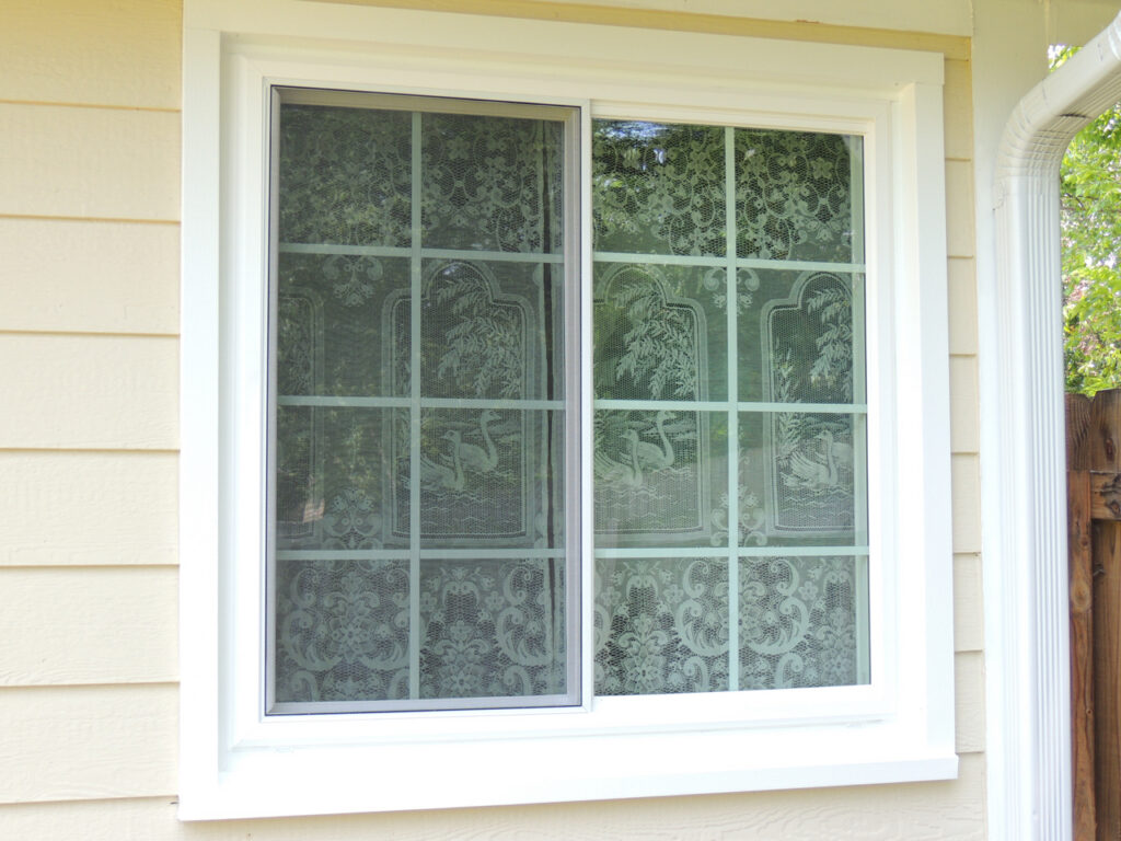 White sliding window with colonial grids and a lace curtain inside.
