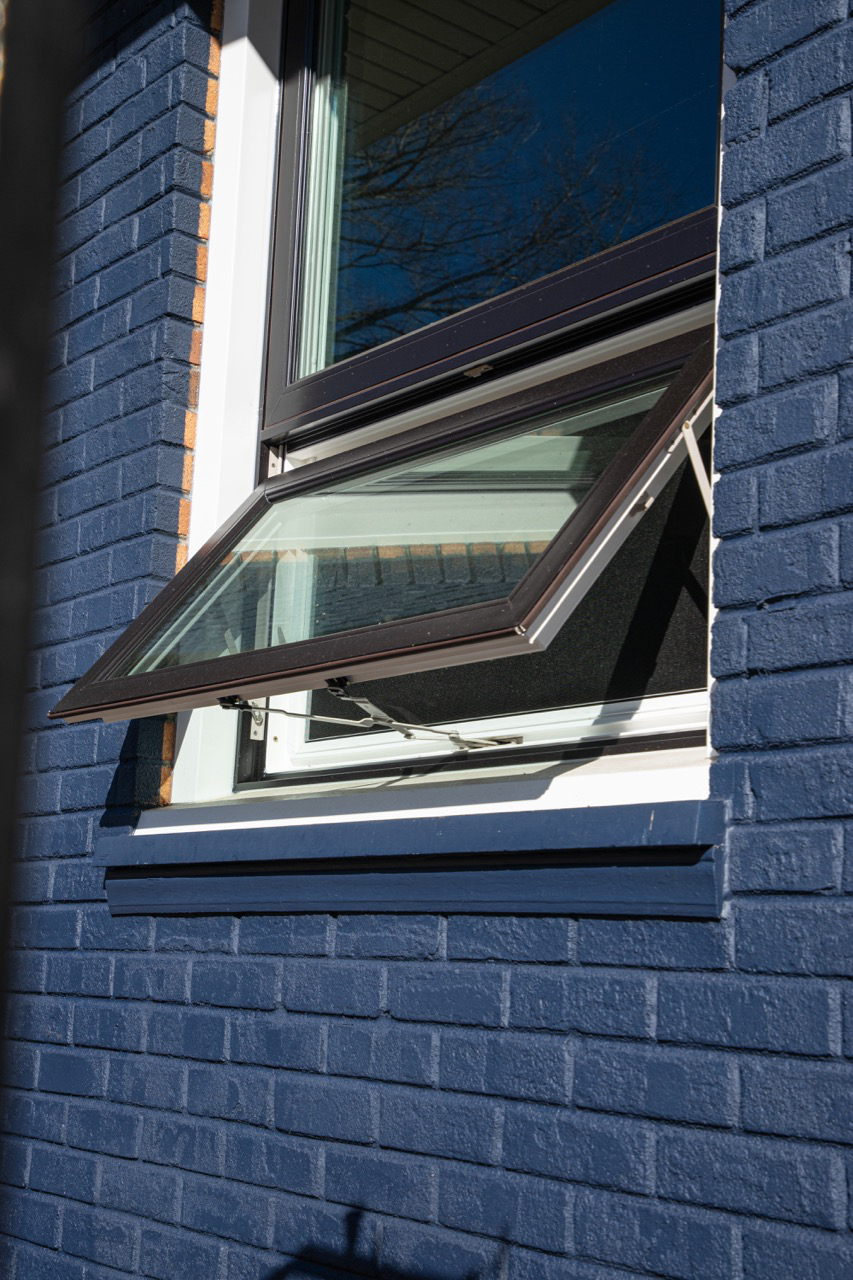 Black open awning window on blue brick house.