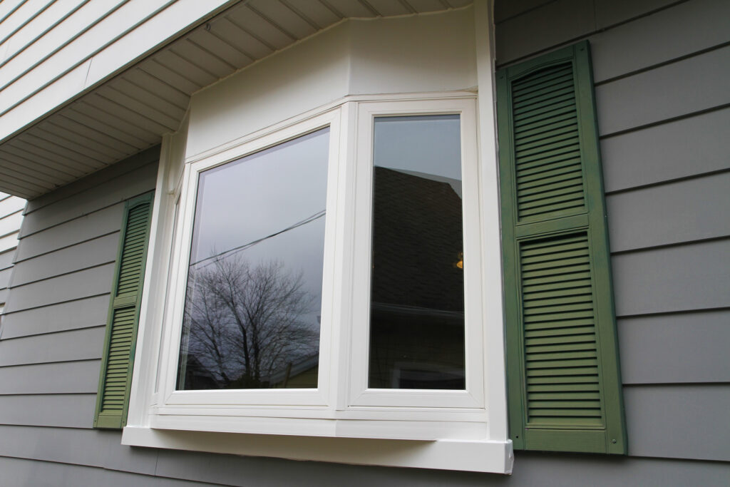 Closeup of white bay window with green shutters.