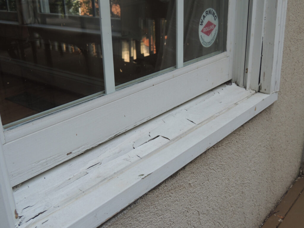 Window frame with chipped paint and wood rot.