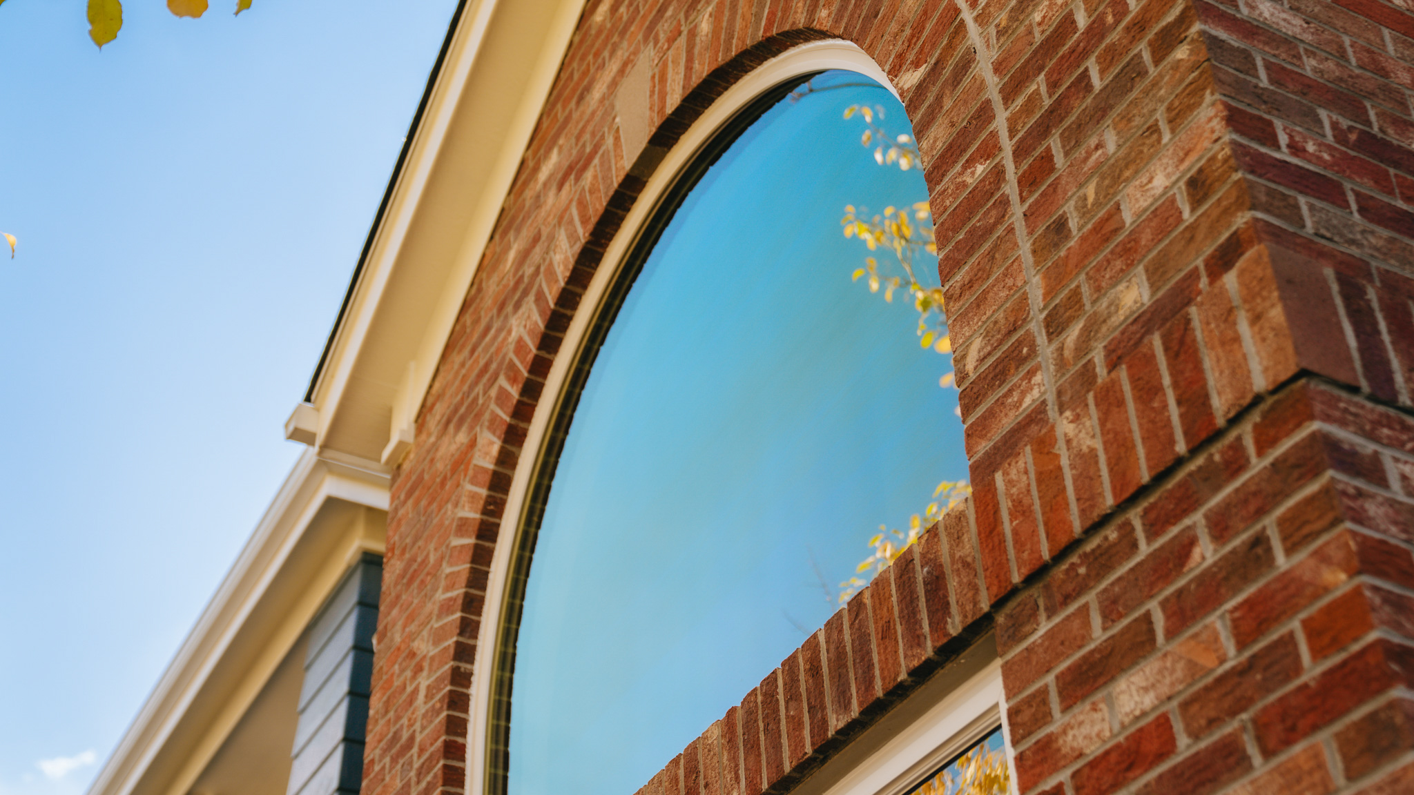 Round top picture window with sky and trees reflected in glass.